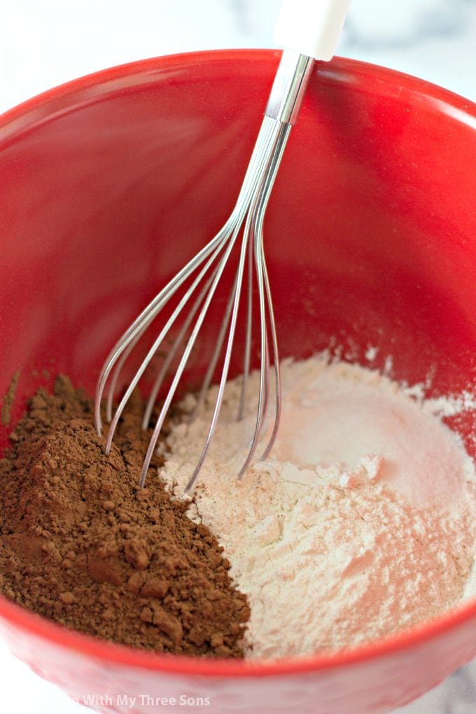 whisking together cocoa powder, flour, and sugar in a red bowl