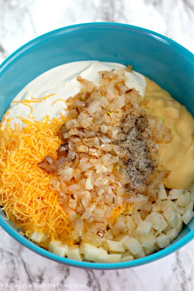 mixing together onions, cheese, sour cream, potatoes, butter, salt, pepper, and cream of chicken soup in a teal bowl