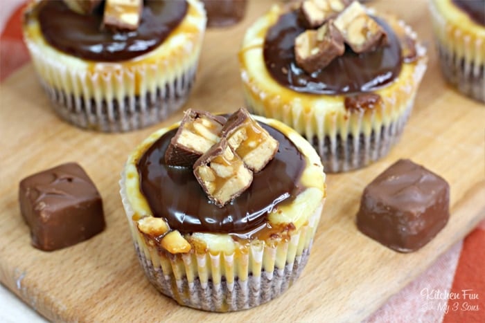 Overhead view of mini Snickers cheesecake bites on a wooden platter next to mini Snickers candies.