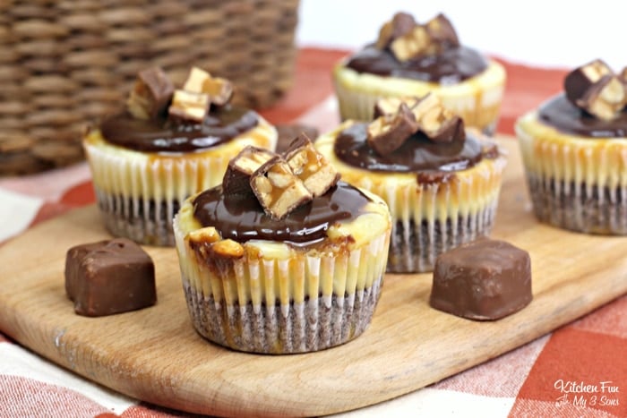 Mini Snickers cheesecake bites on a wooden platter next to mini Snickers candies.