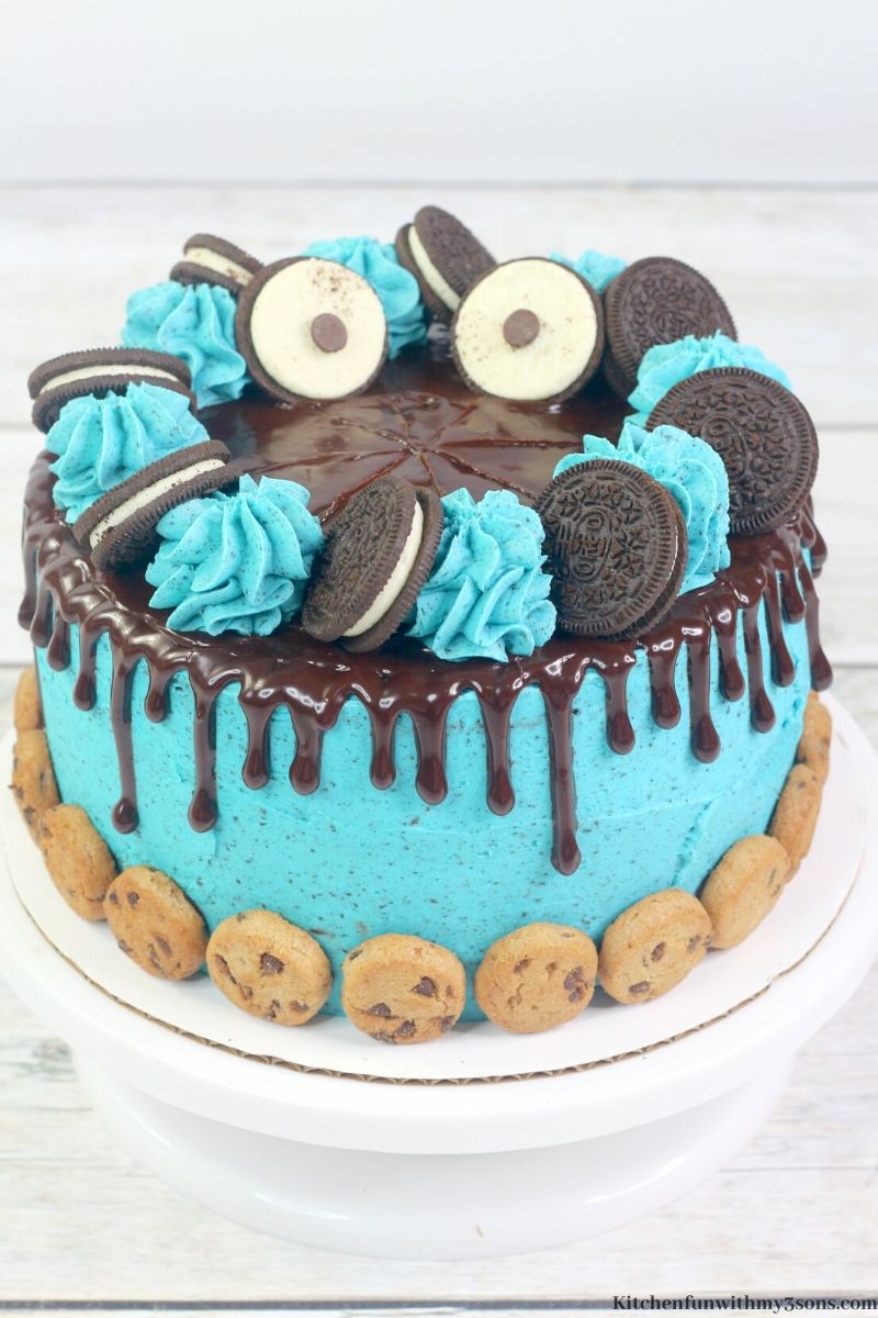 a slice of cookie monster cake on a plate with the full cake in the background