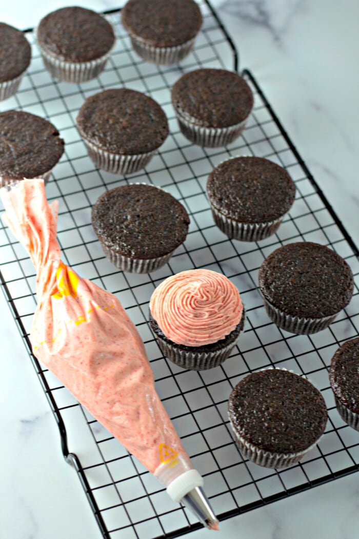 Strawberry frosting piped onto chocolate cupcakes