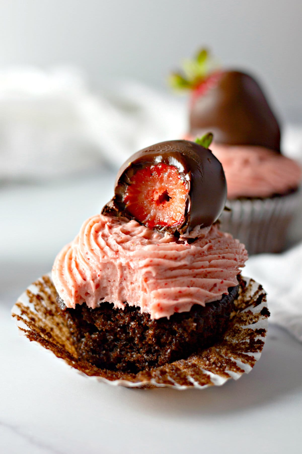 A chocolate covered strawberry cupcake with a bite missing from both the strawberry and cupcake