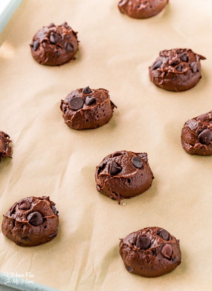 Rows of unbaked pumpkin chocolate  cookie dough balls on a parchment-lined baking sheet.