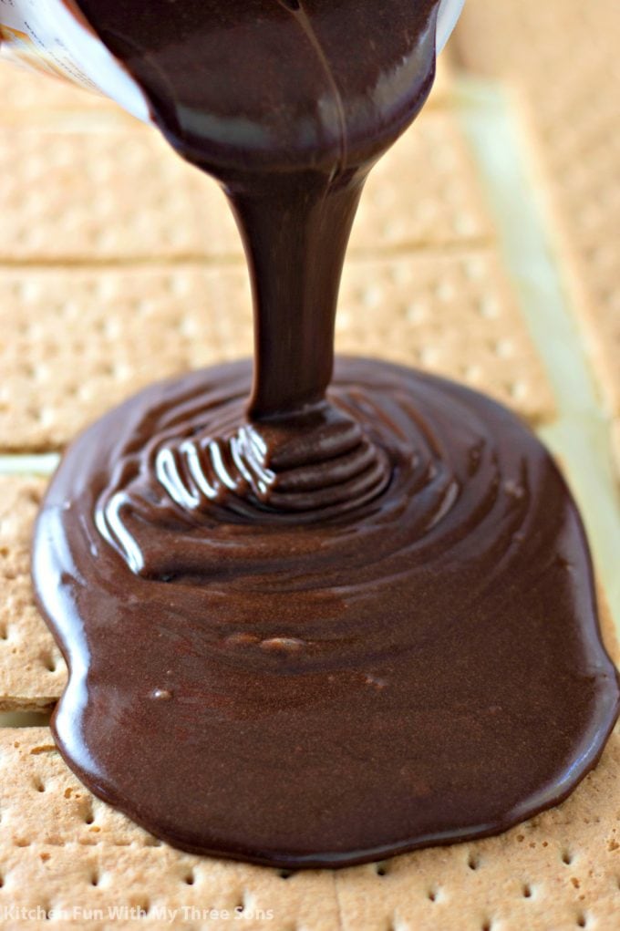 pouring melted chocolate frosting over the eclair cake