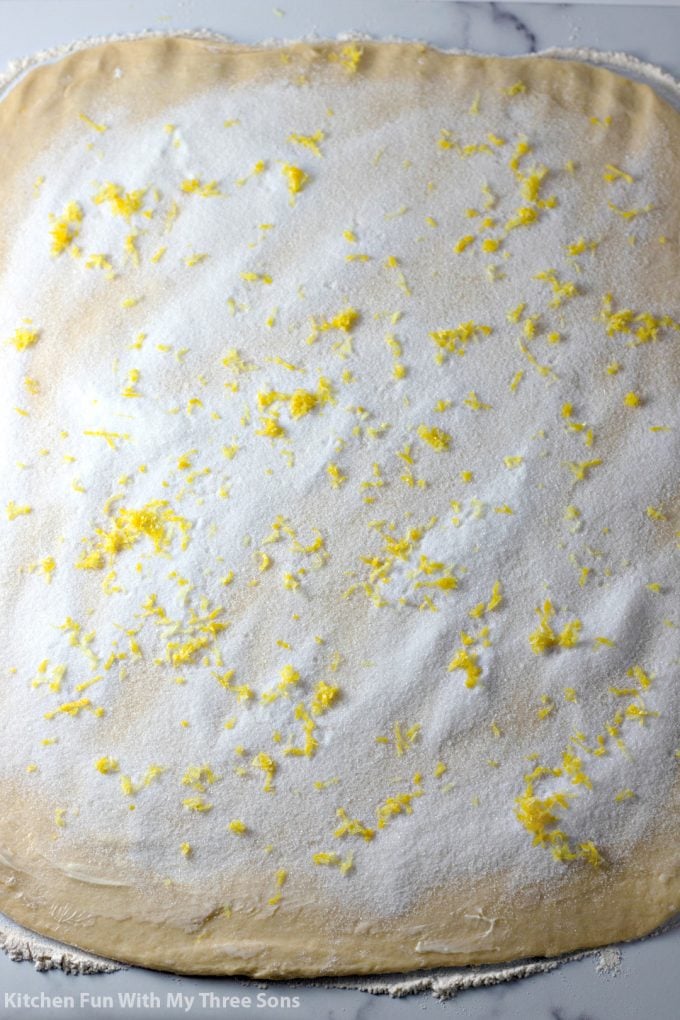 dough rolled out on a counter and topped with sugar and lemon zest