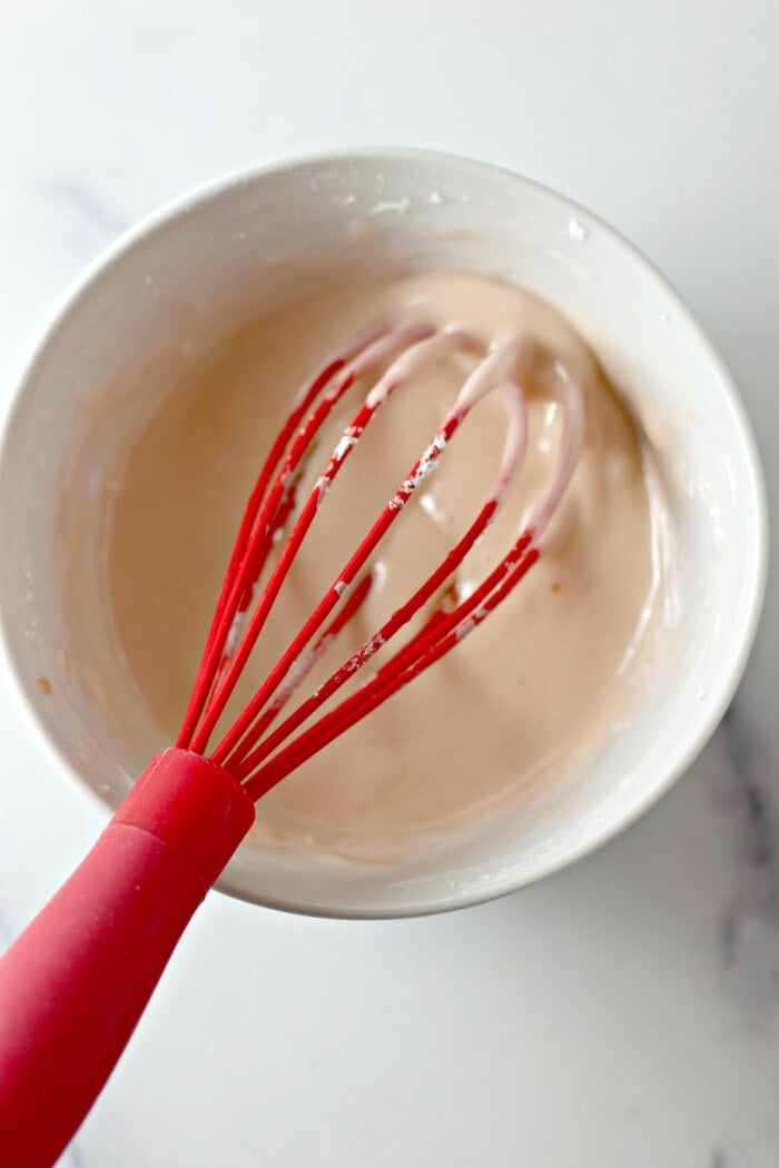 Glaze whisked together in a white bowl with a red rubber whisk.