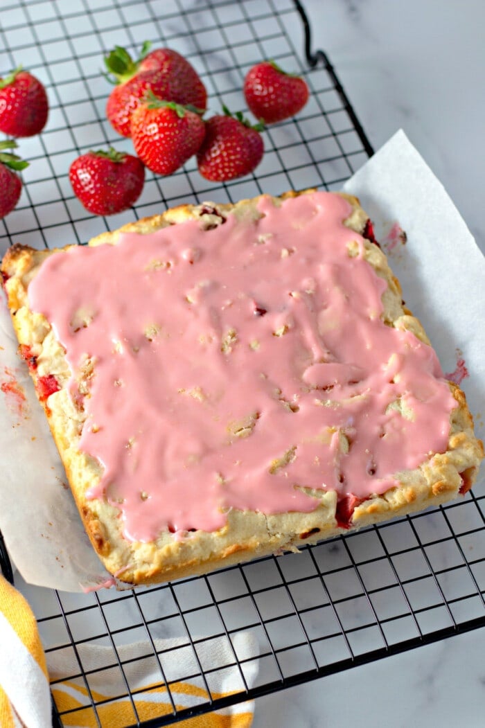 Glazed strawberry lemon blondies on a parchment-lined wire rack, next to fres strawberries.
