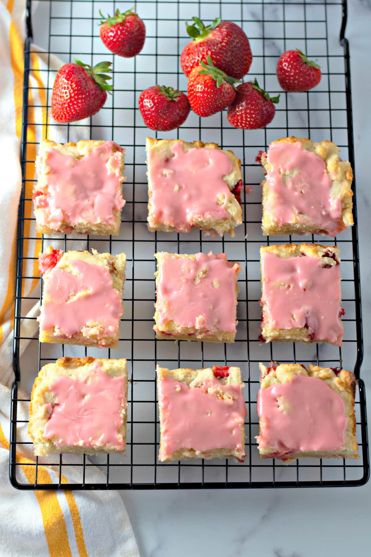 Rows of frosted strawberry lemon blondies on a wire rack next to fresh strawberries.