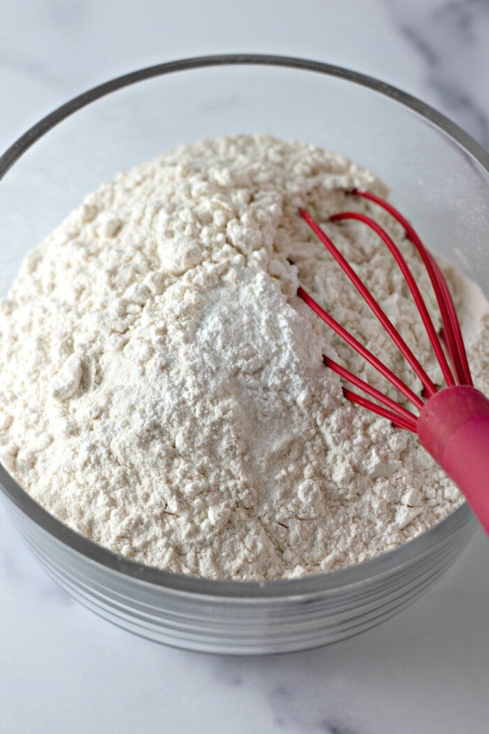Dry ingredients combined in a glass bowl with a red rubber whisk.