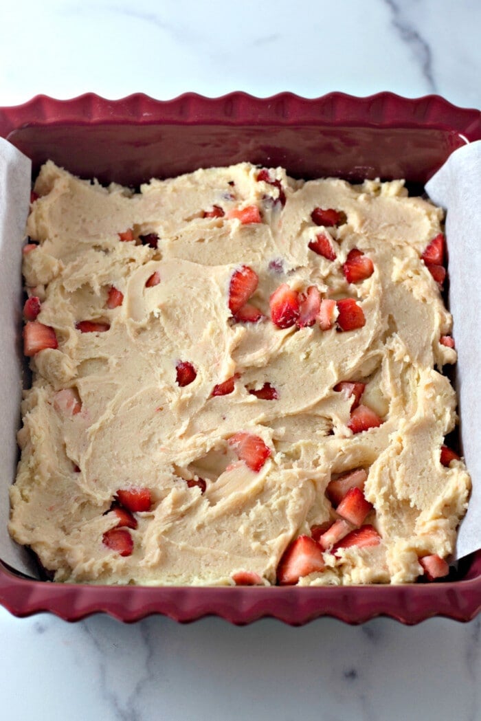Strawberry lemon blondie batter spread into the bottom of a red silicone baking pan lined with parchment paper.