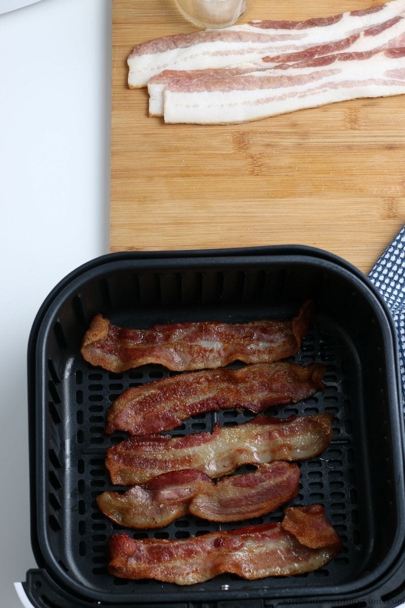 Bacon crisping up in the basket of an air fryer.