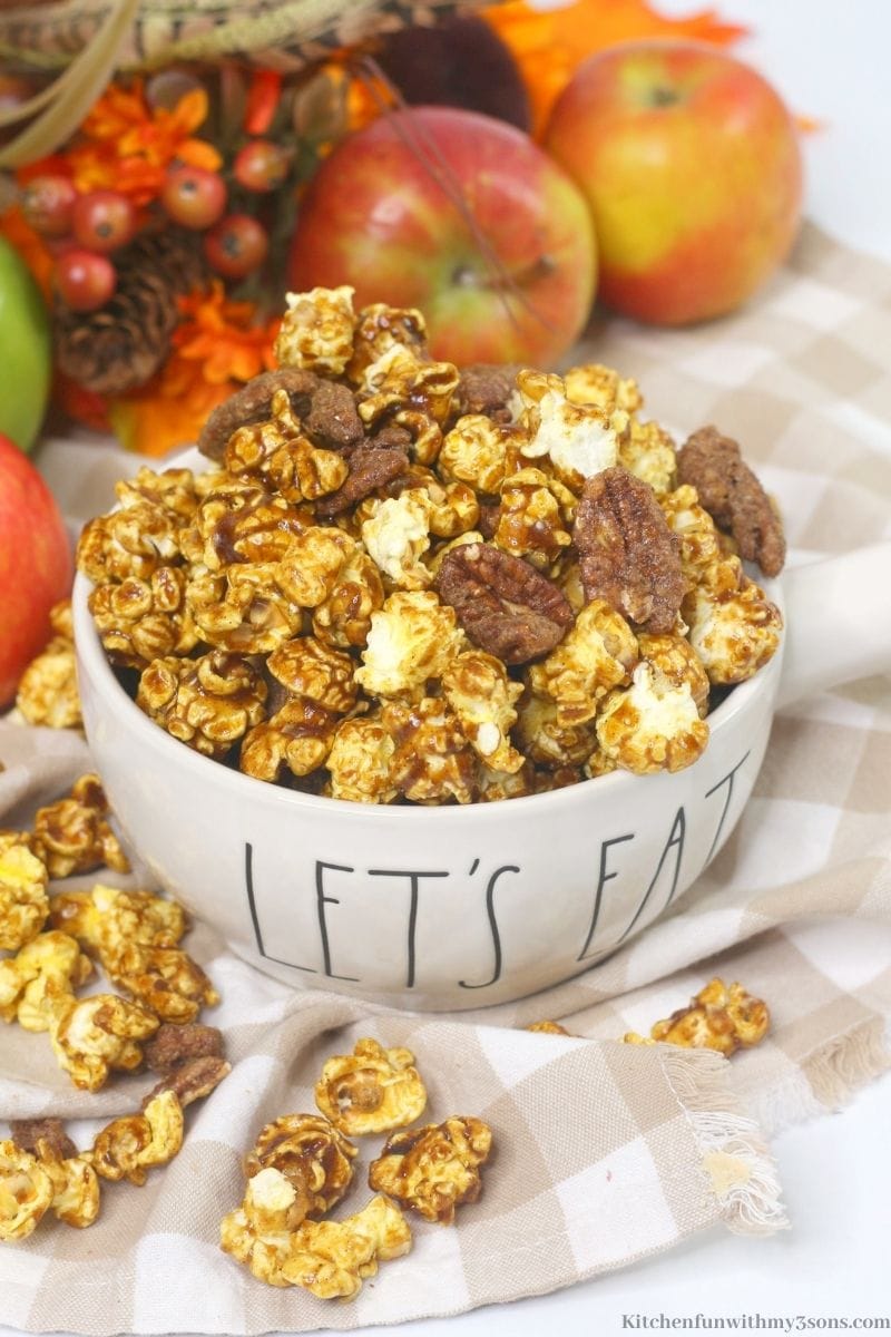 Apple Pie Bourbon Flavored Popcorn Mix with apples, twigs and leaves behind it.
