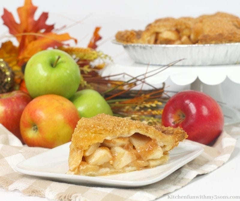 Autumn leaves and a pile of fresh apples behind a plate with a pie slice on it.