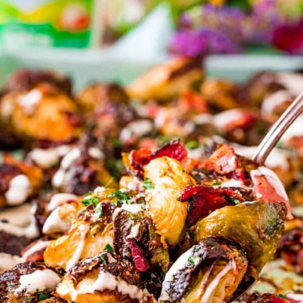 Close up of a spoon scooping up a serving of Brussels sprouts with bacon from a tray.