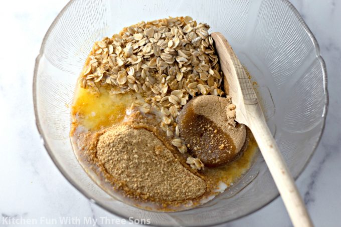 mixing together cheesecake crust ingredients in a clear bowl with a wooden spoon