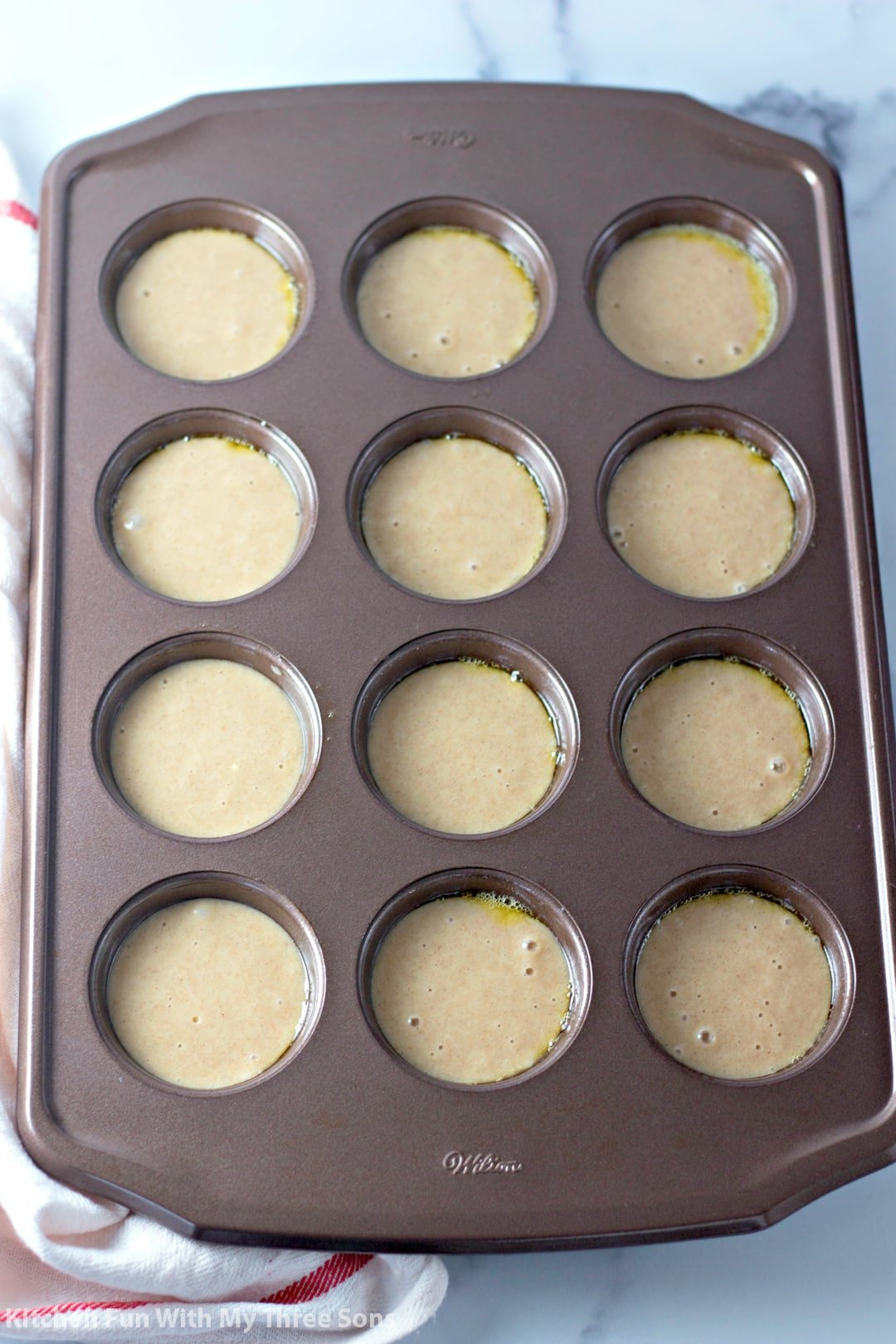 A muffin tin filled with batter on top of a cloth napkin on a marble countertop