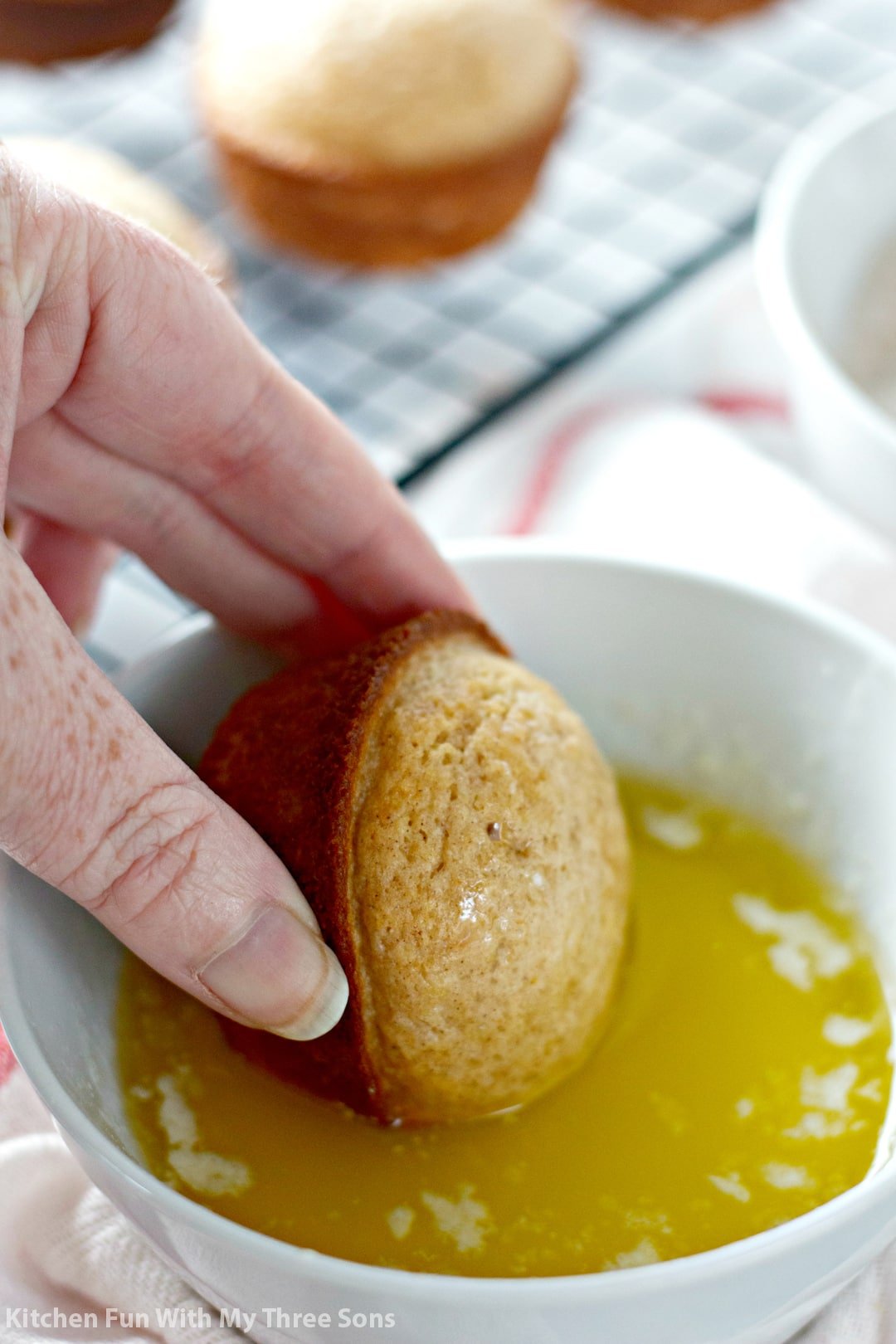 A cooled muffin being dipped into a bowl of melted butter