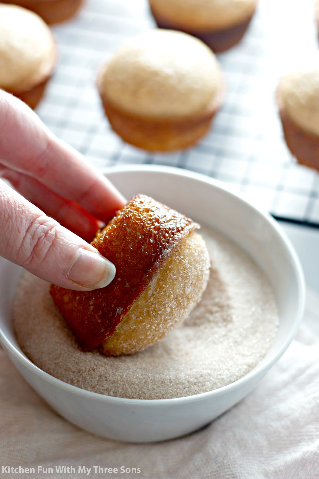 A butter-coated donut muffin being dipped into a bowl of cinnamon sugar