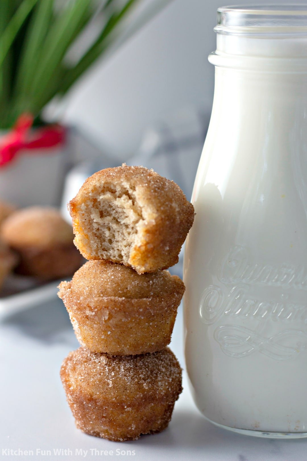 Three stacked cinnamon sugar muffins leaning against a jar full of milk