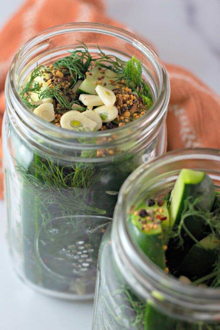 adding garlic and herbs to cucumbers in jars
