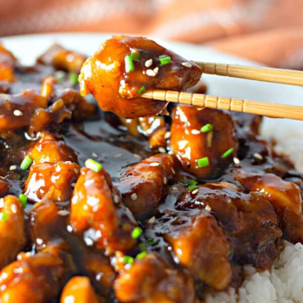 Chopsticks holding a piece of bourbon chicken