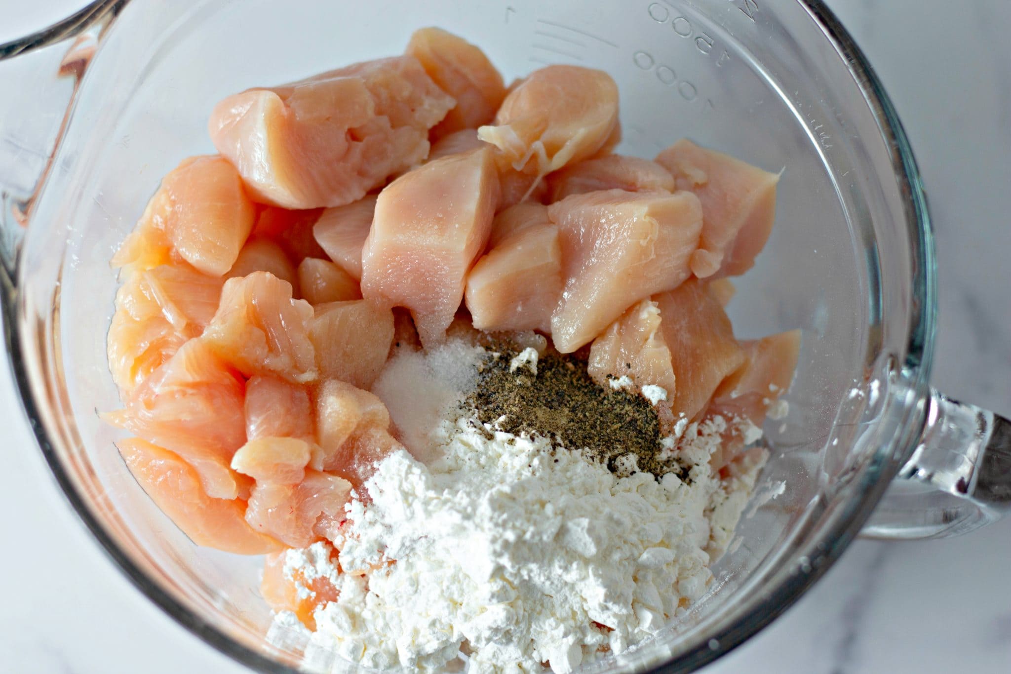 Chunks of raw chicken, cornstarch, and seasonings in a bowl