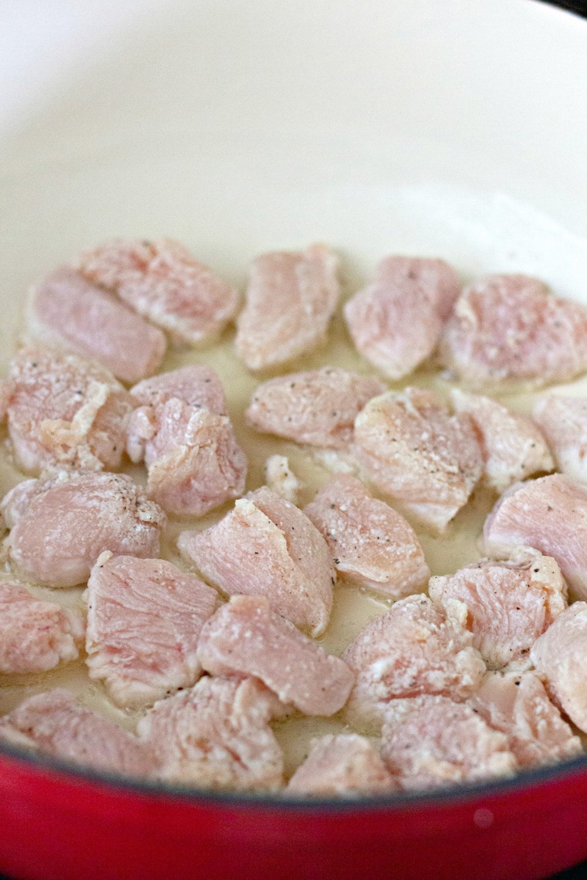 Chunks of chicken frying in oil in a pan