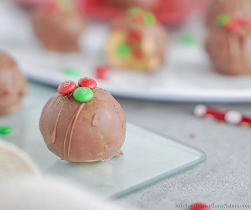 Christmas Peanut Butter Balls on a glass sheet with festive straws and more behind it.