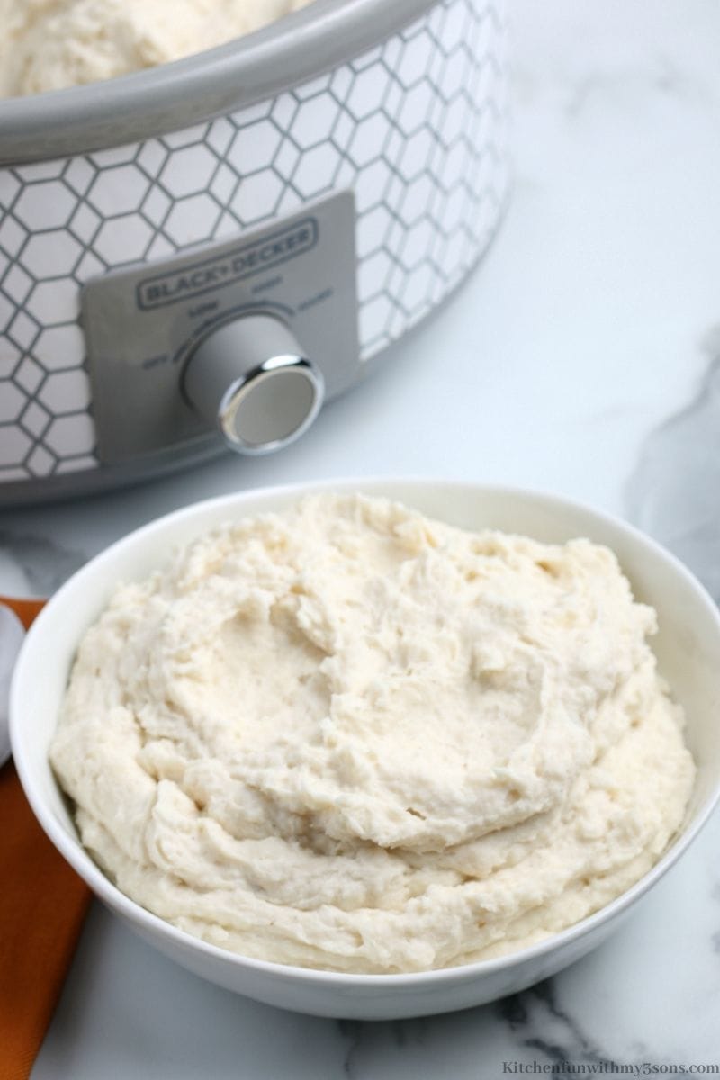 A bowl of crock pot mashed potatoes in front of the crockpot