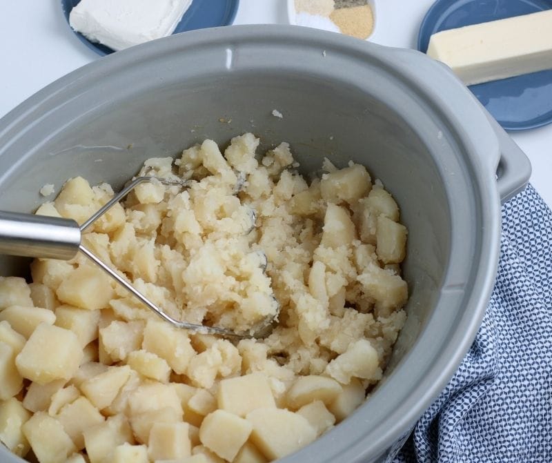 The potatoes being mashed with a potato masher.