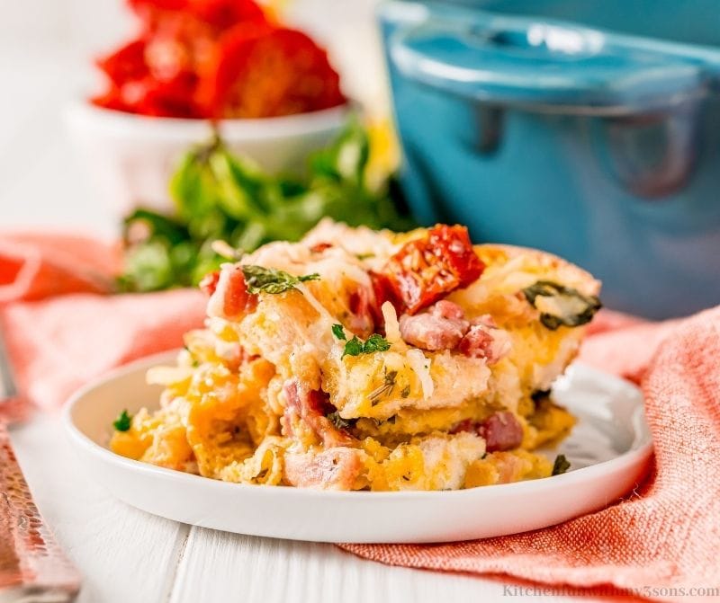 Easy Italian Breakfast Casserole on a dish on a red cloth with the baking pan behind it.