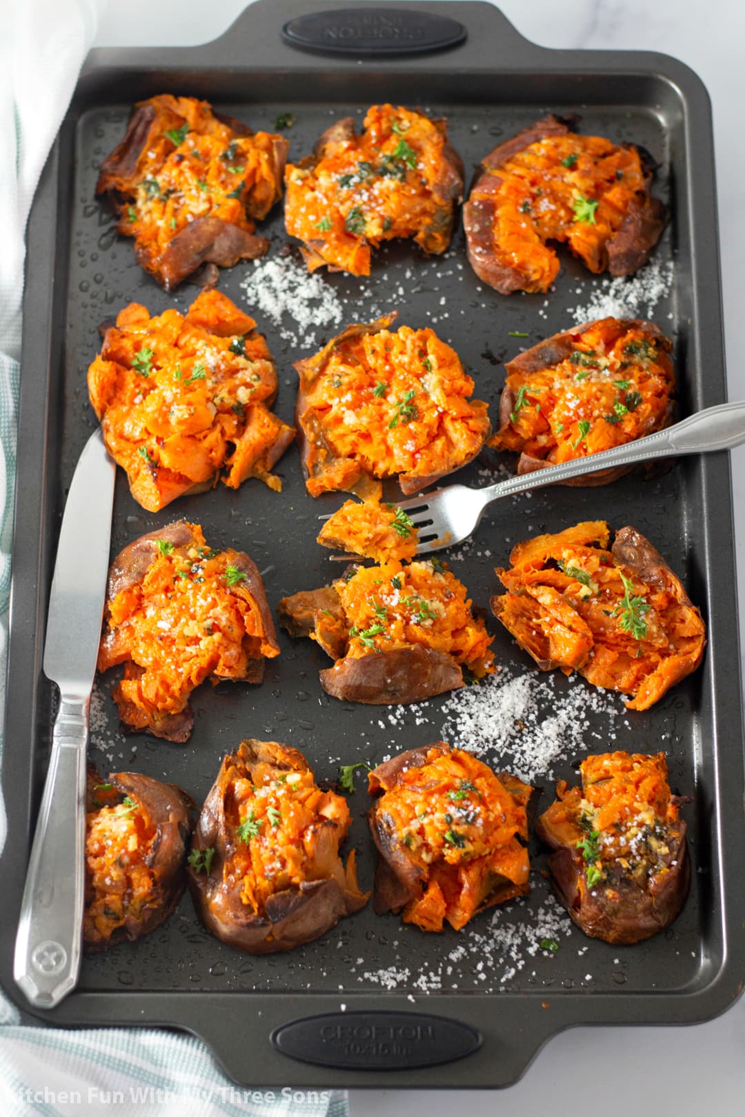 Garlic Butter Smashed Sweet Potatoes on a cookie sheet with a knife and fork