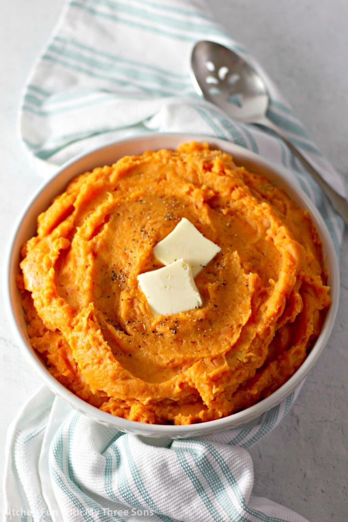 a bowl of Mashed Sweet Potatoes with a pat of butter on top and a blue and white towel next to the bowl