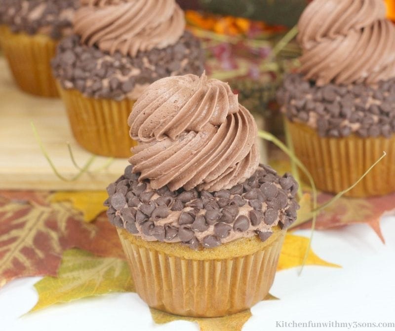 Pumpkin Chocolate Chip Cupcakes with more cupcakes behind in on a wooden board.