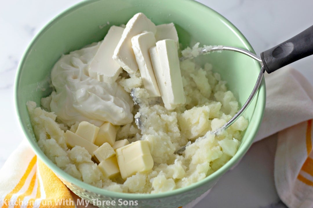 Cream cheese, sour cream, and butter added to mashed potatoes in a green boil