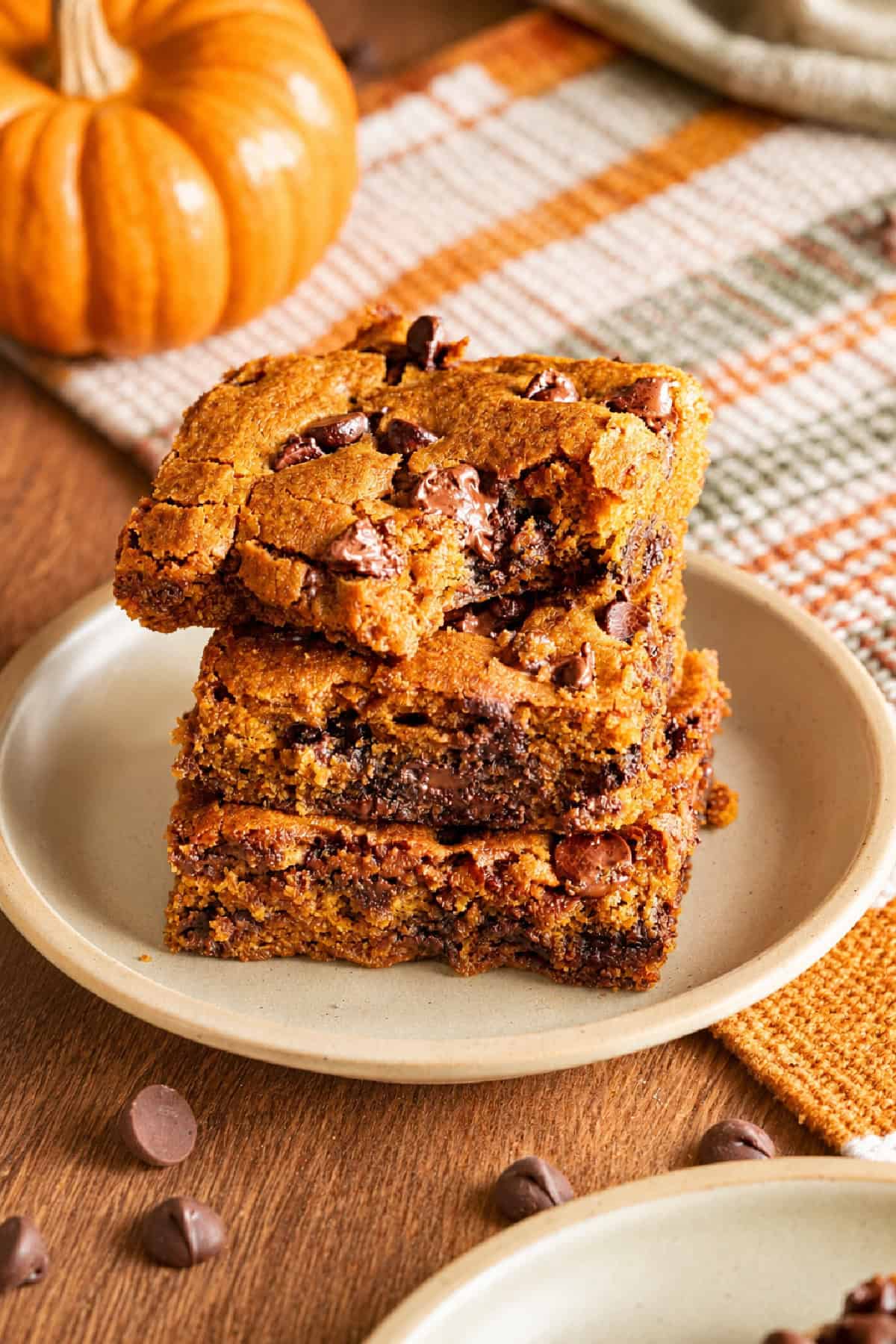 These Pumpkin Chocolate Chip Bars are soft, moist, and packed with cozy Fall flavor and melty chocolate chips! Pumpkin Chocolate Chip Cookies stacked on a plate