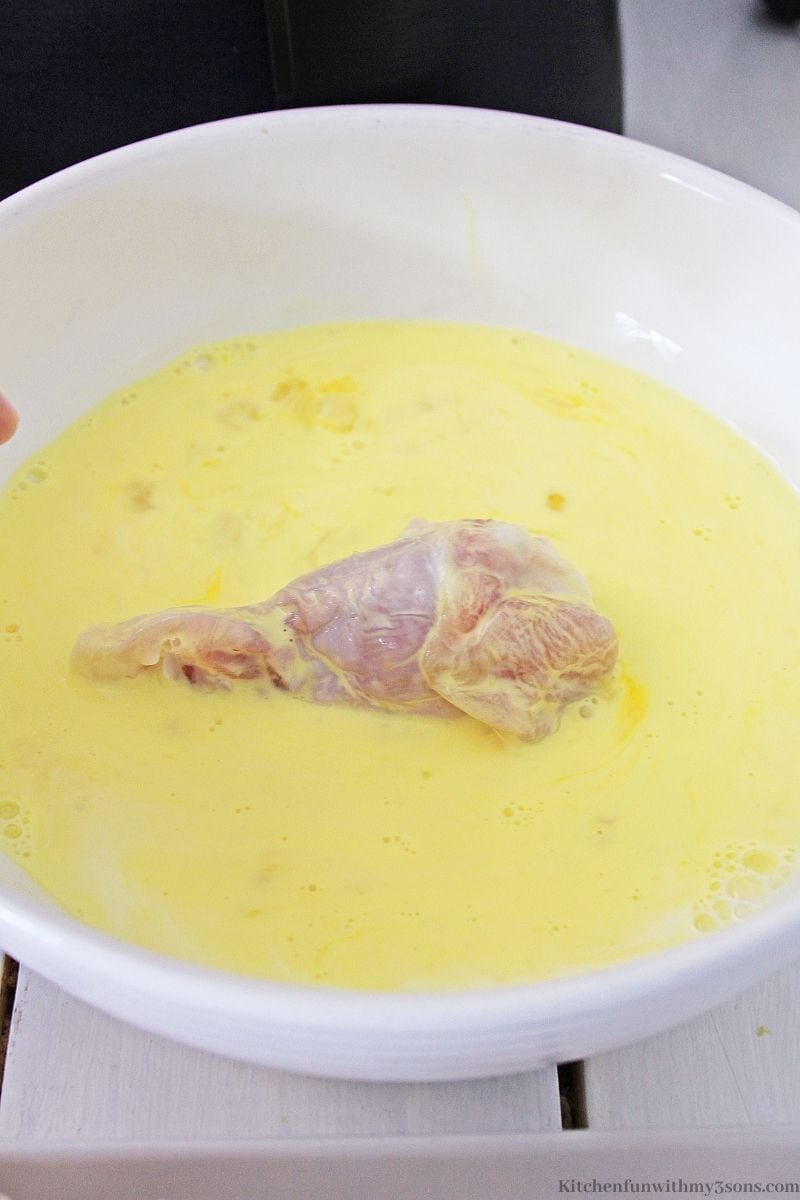 The raw wing being dipped into the egg and milk mixture.