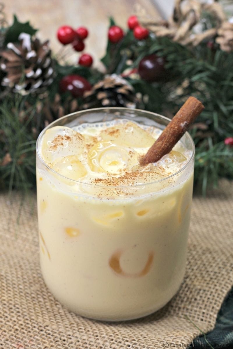 Amaretto Eggnog Cocktail with snow frosted branches and pine cones behind it.