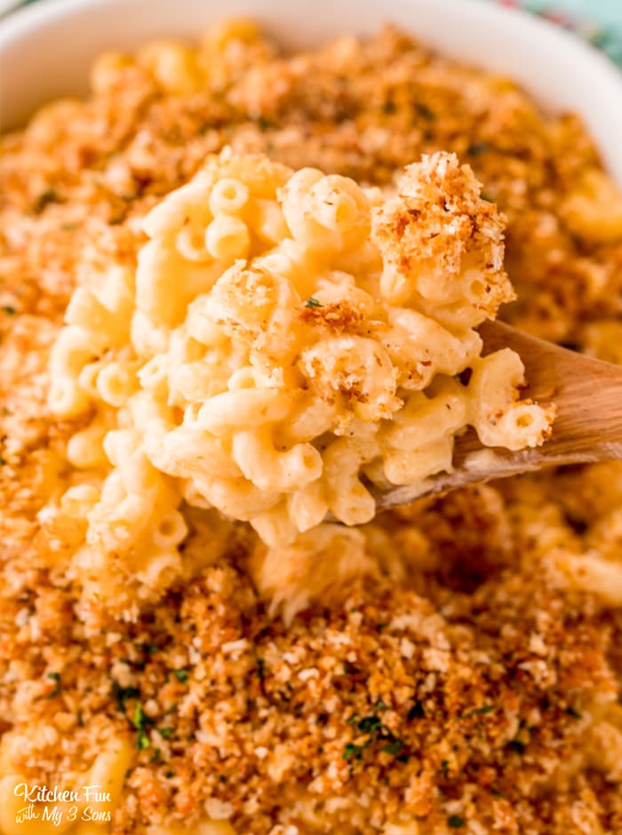 Baked macaroni and cheese on a wooden spoon over a casserole dish 