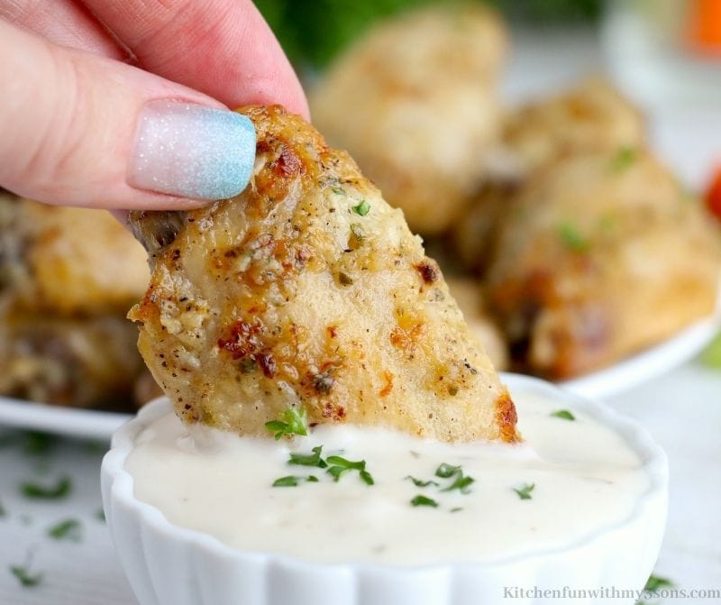 Dipping the finished Baked Ranch Chicken Wings into a dipping sauce.