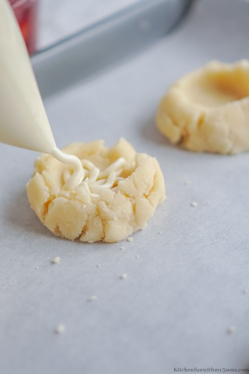 Piping the cream cheese filling into the indent in the center of the cookie.