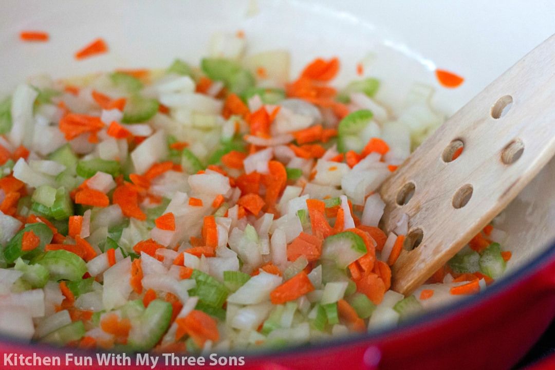 Diced celery, carrots, and onions are sauteed in a saucepan.