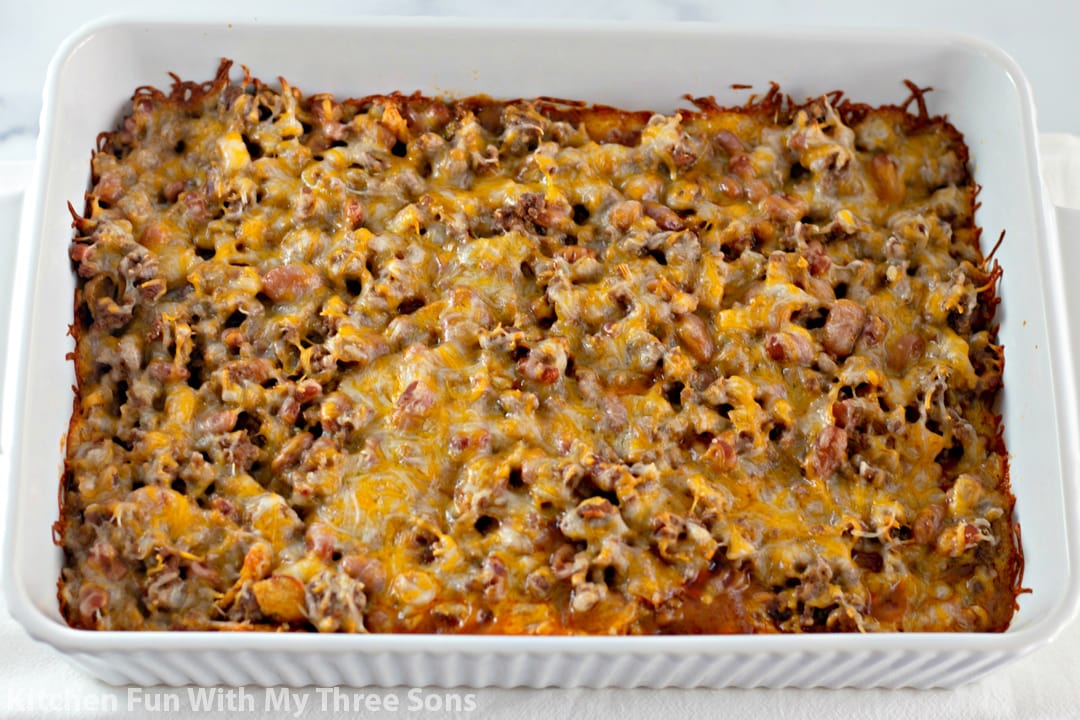 A baked Frito pie, not yet garnished with additional Frito chips. The melted cheese and chili are visible in the white casserole dish.