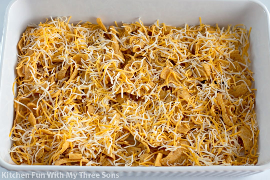 A casserole dish with a layer of Fritos in the bottom, and a layer of shredded cheese over the Fritos.