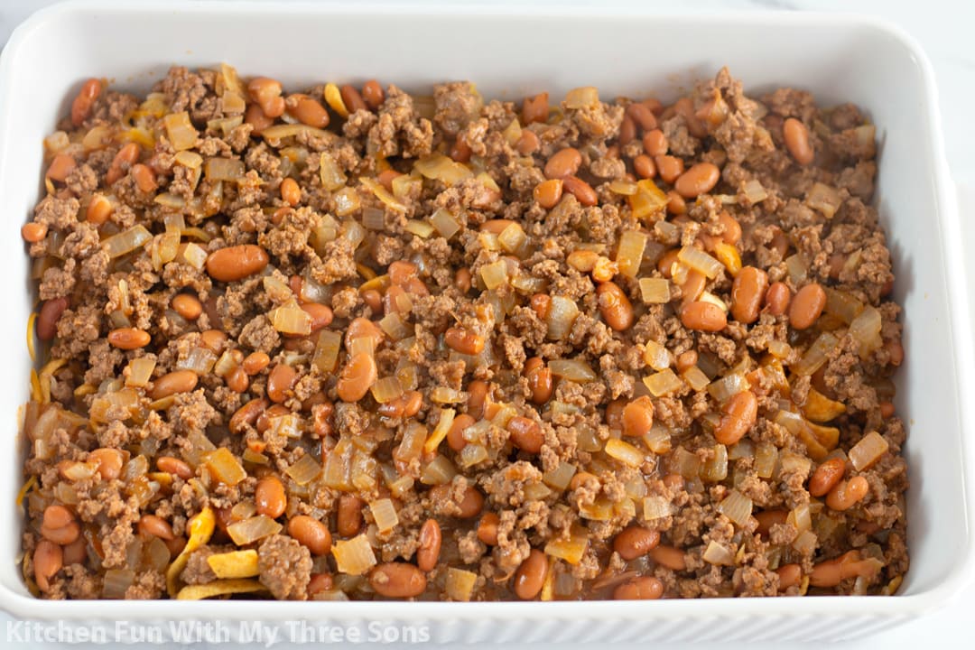 A casserole dish filled with Fritos, shredded cheese, and a layer of chili.