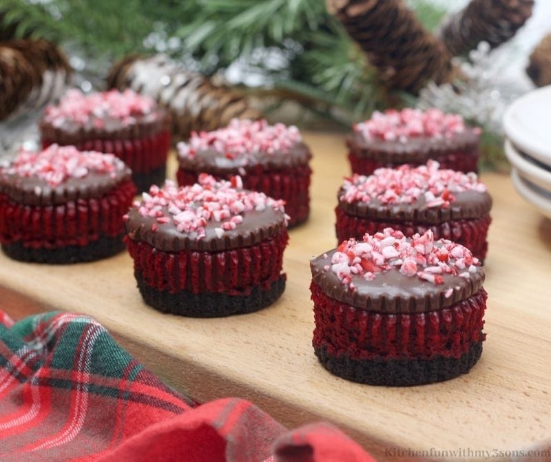 Mint Red Velvet Mini Cheesecakes with wood decorations in the back on a patterned cloth.