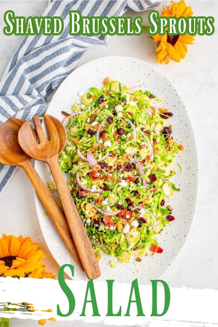 Shaved Brussels Sprouts Salad with bacon on a white platter and two wooden salad spoons on the side with a striped napkin