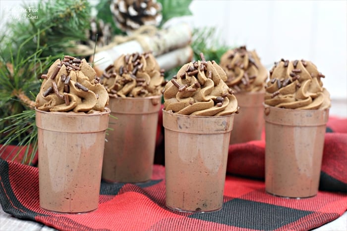 Five mocha pudding shots on top of a red and black placemat with pine needles and pine cones behind them