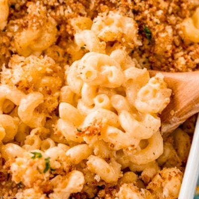 Baked mac and cheese on a wooden spoon over a casserole dish